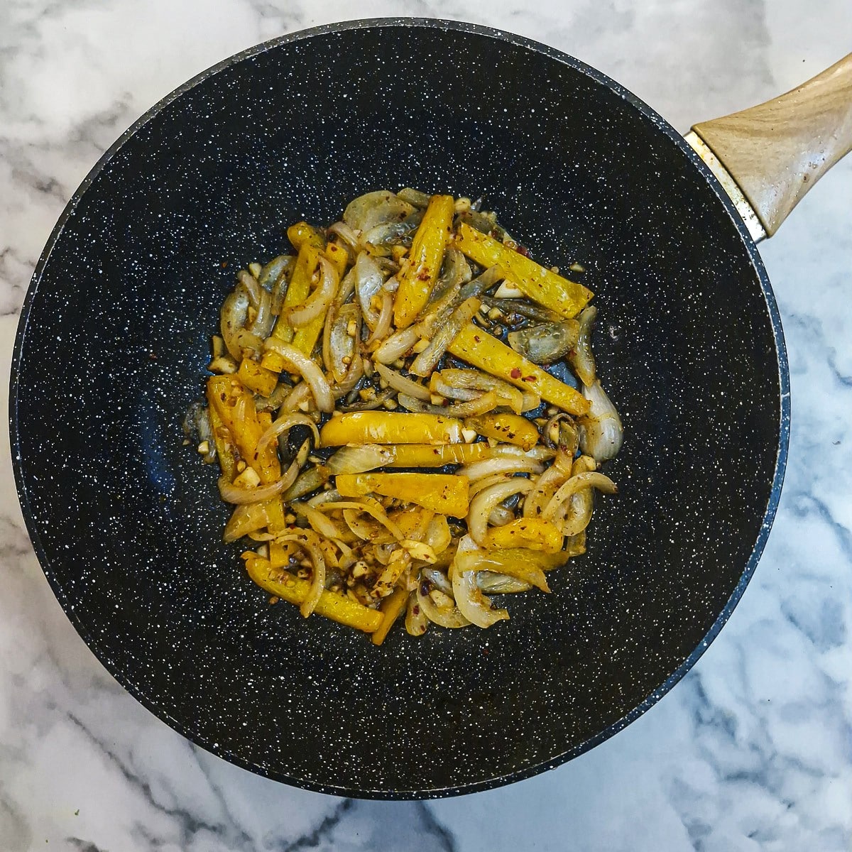 Sliced onions and capsicum softening in a wok.