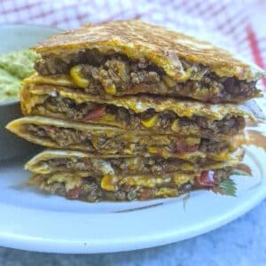 A pile of 5 slices of beef and corn quesadillas on a white plate.