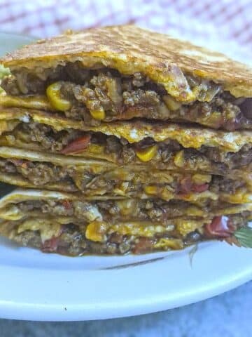 A pile of 5 slices of beef and corn quesadillas on a white plate.