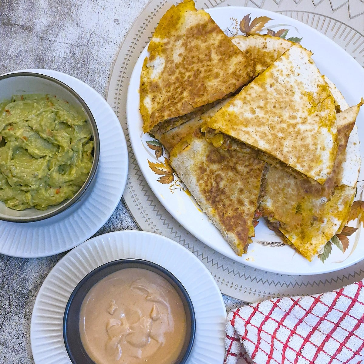 Slices of beef and corn quesadilla on a plate alongside a bowl of quacamole and a bowl of tangy Marie Rose sauce.