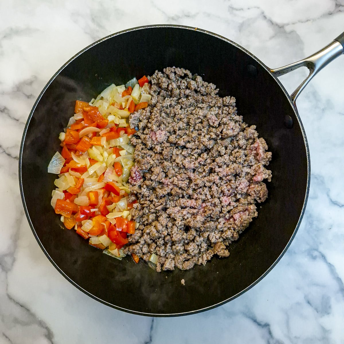 Peppers and onions pushed to one side of the pan and ground beef added and browned.