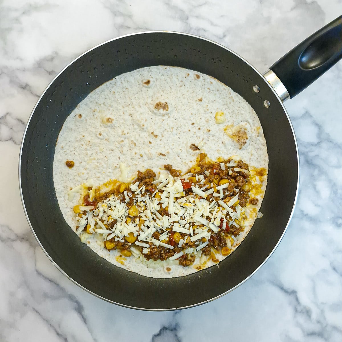 Mince and cheese arrqanged on one side of a tortilla in a frying pan.