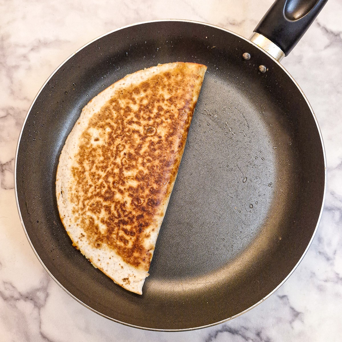 A cheesy beef quesadilla browned on both sides in a frying pan.
