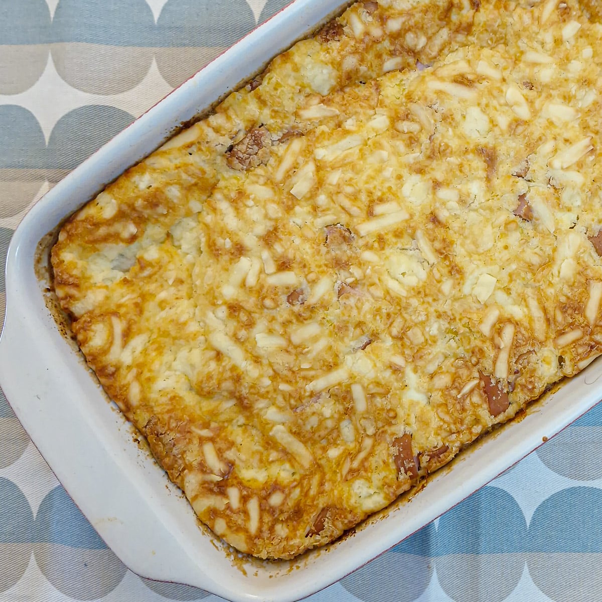 Close up of the egg and sausage savoury tart in the baking dish., showing the melted gooey cheese on top.