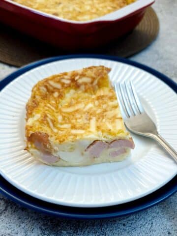 A slice of crustless egg and sausae tart on a white plade with a cake fork.