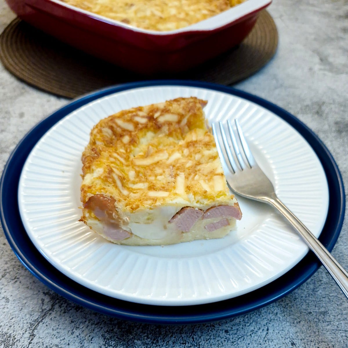A slice of crustless egg and sausae tart on a white plade with a cake fork.