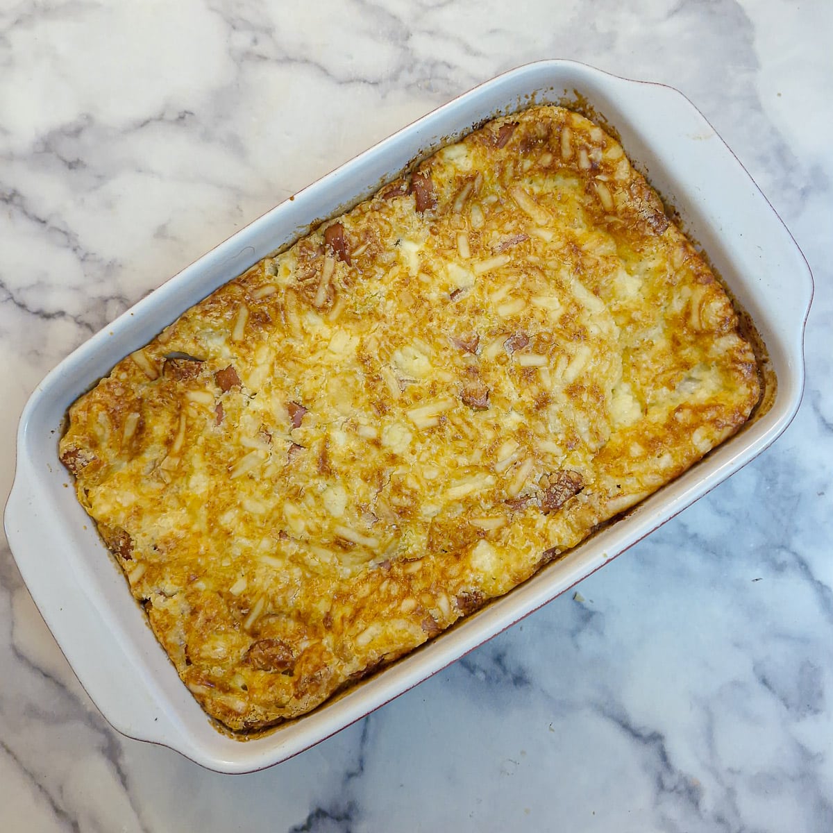 A golden brown baked crustless egg and sausage savoury tart in a white baking dish.