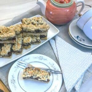 A tea tray laid with a plate of date and walnut crumble bars. A teapot, 2 cups and saucers and a slice of the date bar on a plate are also on the tray.