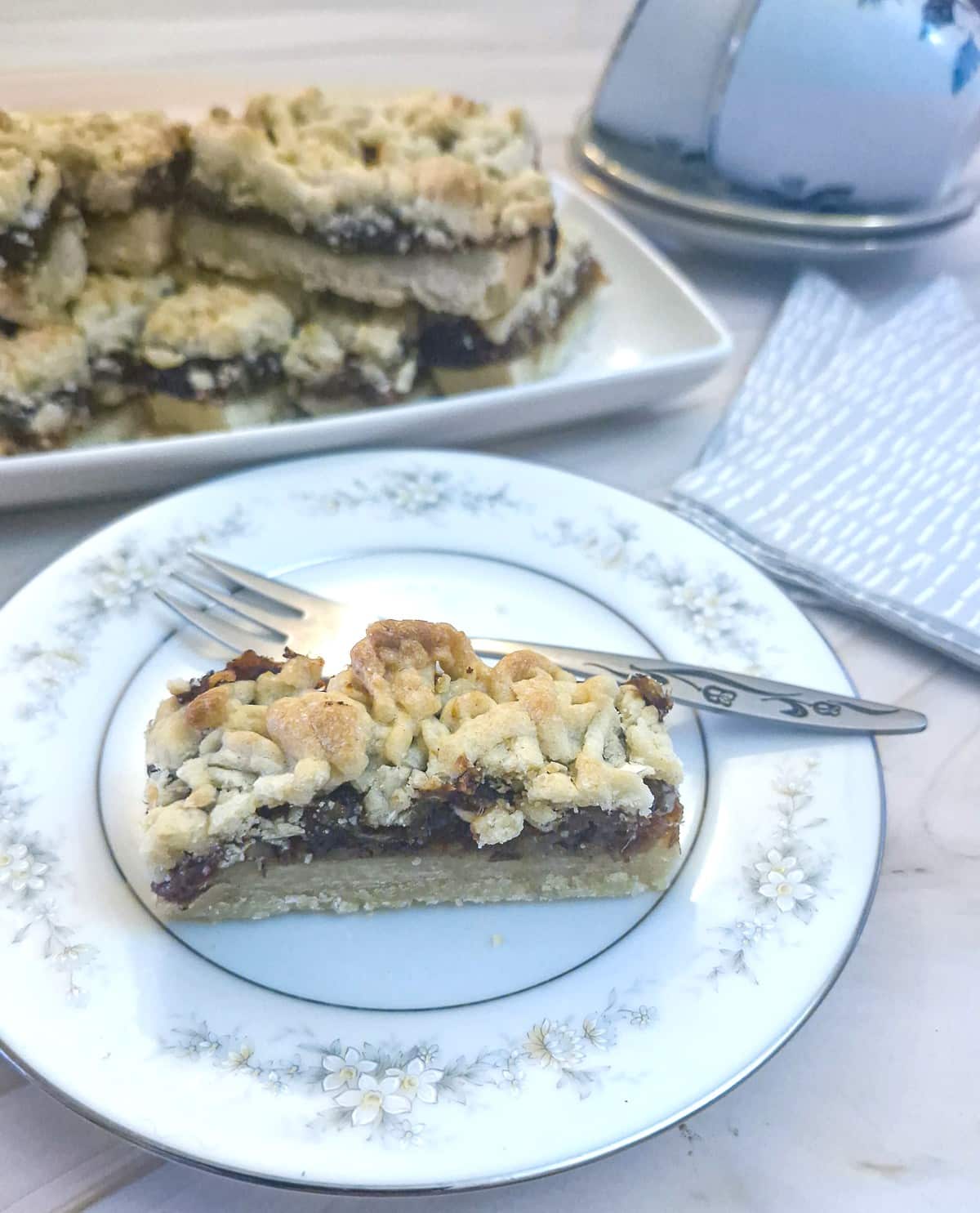 Close up of a slice of date and walnut crumble on a blue patterned side plate with a cake fork.
