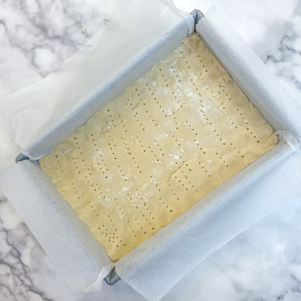 Pastry that has been pricked with a fork in the base of a baking tray.