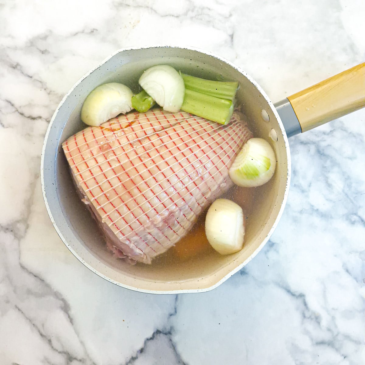 Gammon and vegetables covered with water in a large saucepan.
