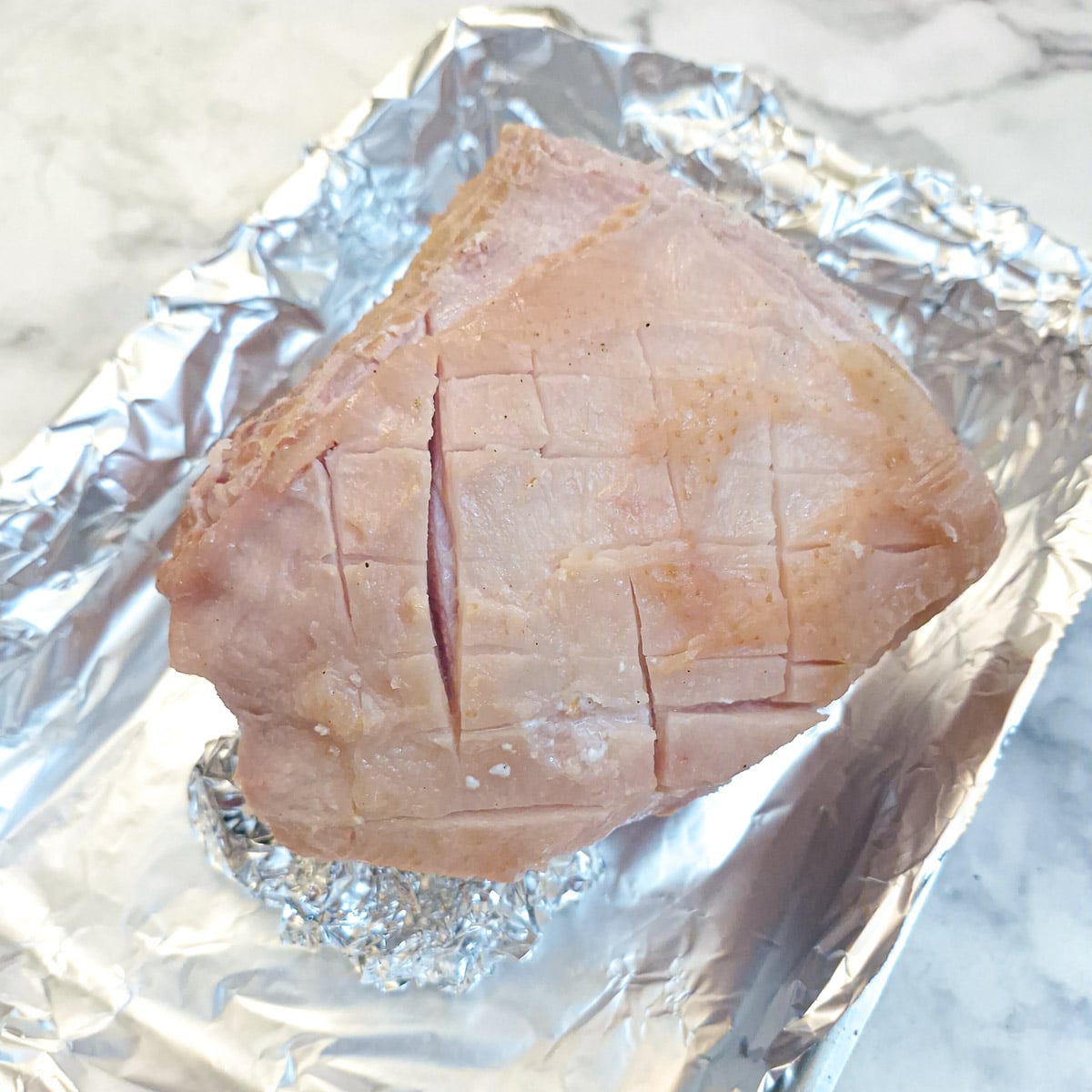 The skinned boiled gammon in a roasting dish. The fat has been scored into a shallow diamond pattern.