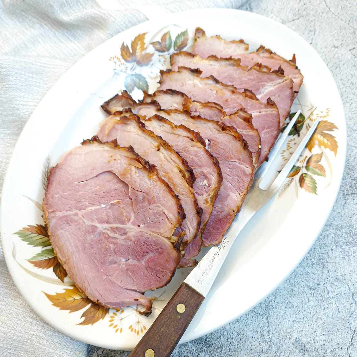 Sliced ham on a serving plate with a large fork.