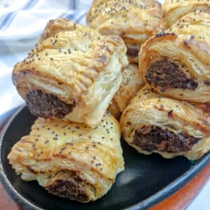 A pile of mushroom sausage rolls garnished with black poppy seeds on a serving dish.
