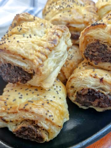 A pile of mushroom sausage rolls garnished with black poppy seeds on a serving dish.