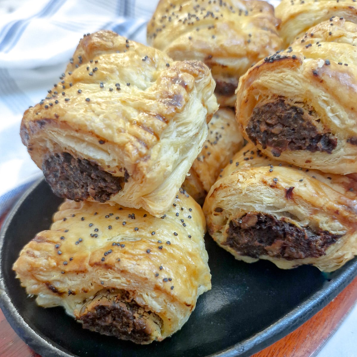 A pile of mushroom sausage rolls garnished with black poppy seeds on a serving dish.