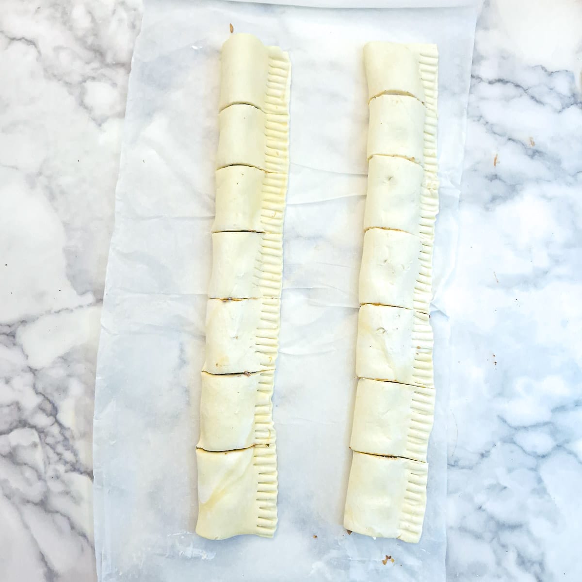 Two rows of sausage rolls brushed with beaten egg.