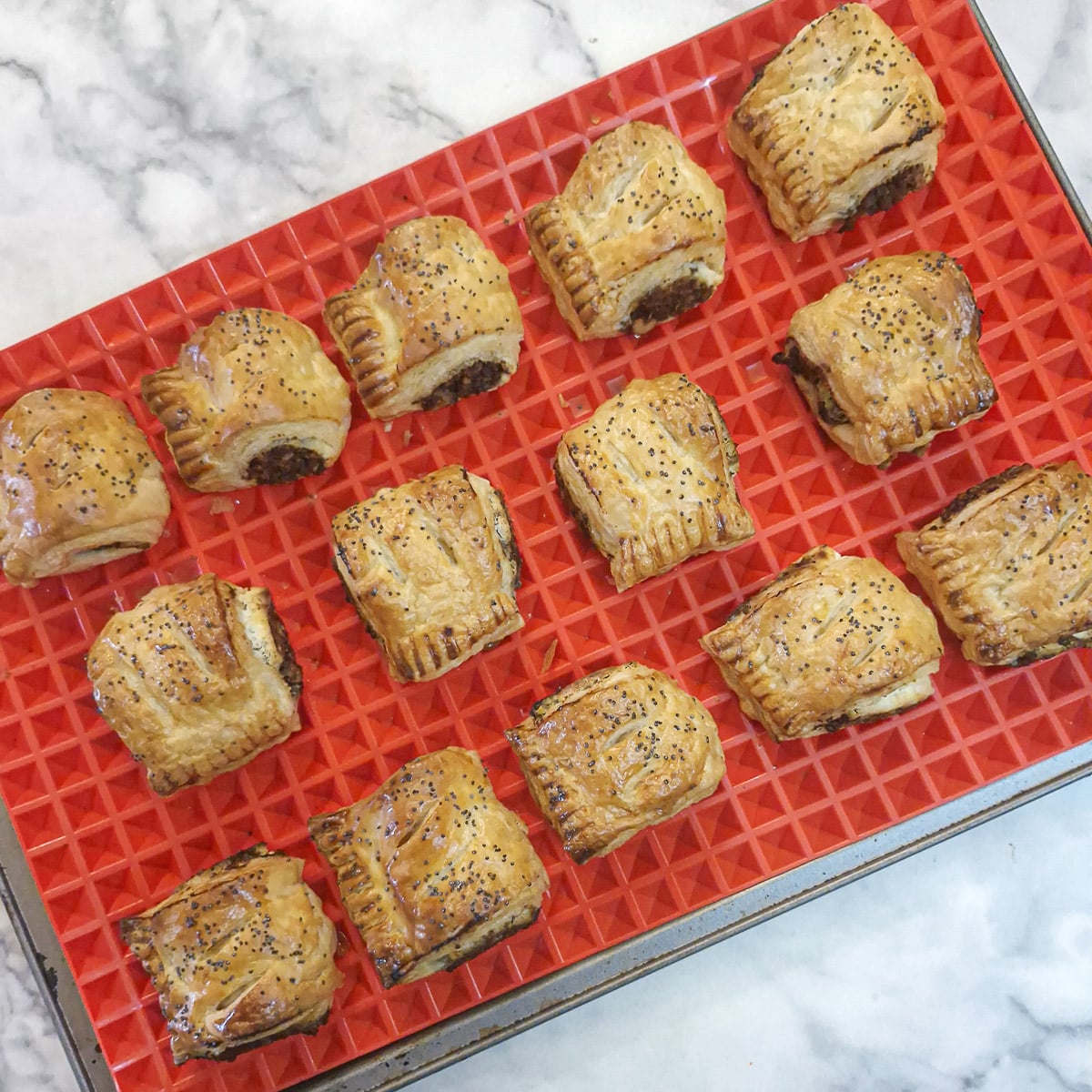 14 baked sausage rolls cooling on a silicone-lined baking tray.