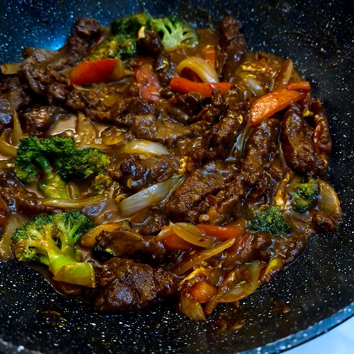 Close up of sweet chilli beef stir fry in a wok, showing how the sauce clings to the meat.