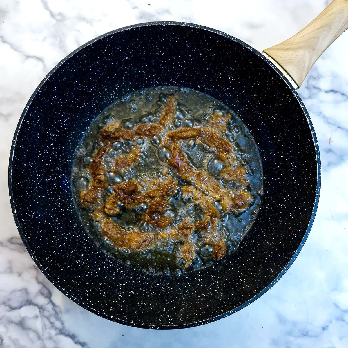 Beef strips frying in oil in a wok.
