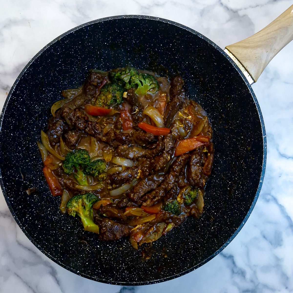 Meat strips and sauce combined with the vegetables in a wok.