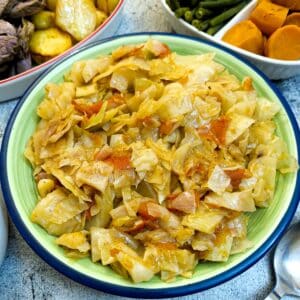 A green serving dish filled with tomato braised cabbage.