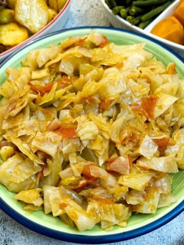 A green serving dish filled with tomato braised cabbage.