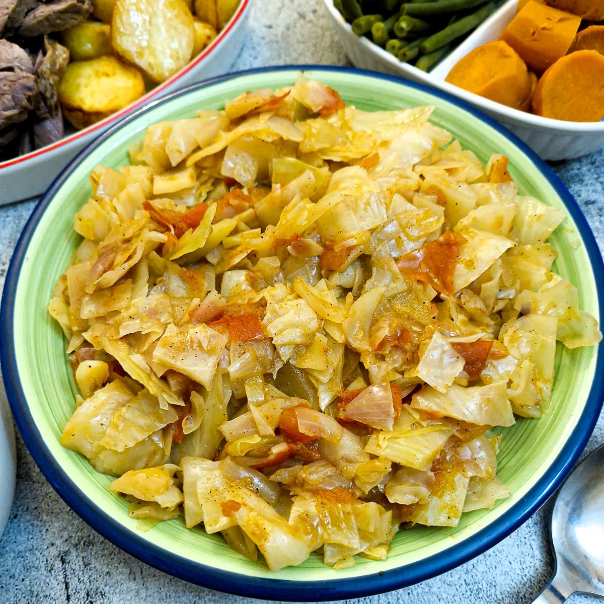 A green serving dish filled with tomato braised cabbage.