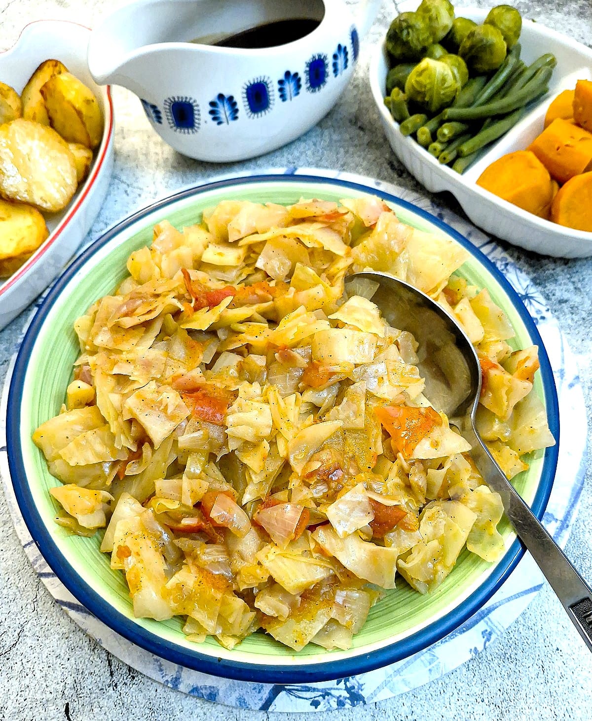 Tomato-braised cabbage in a serving dish on a table, surrounded by other dishes of vegetables.