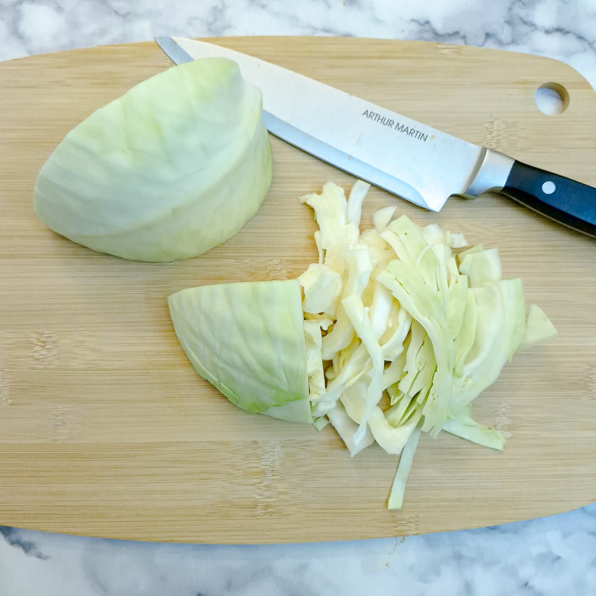 Sliced cabbage on a chopping board with a large knife on the side.