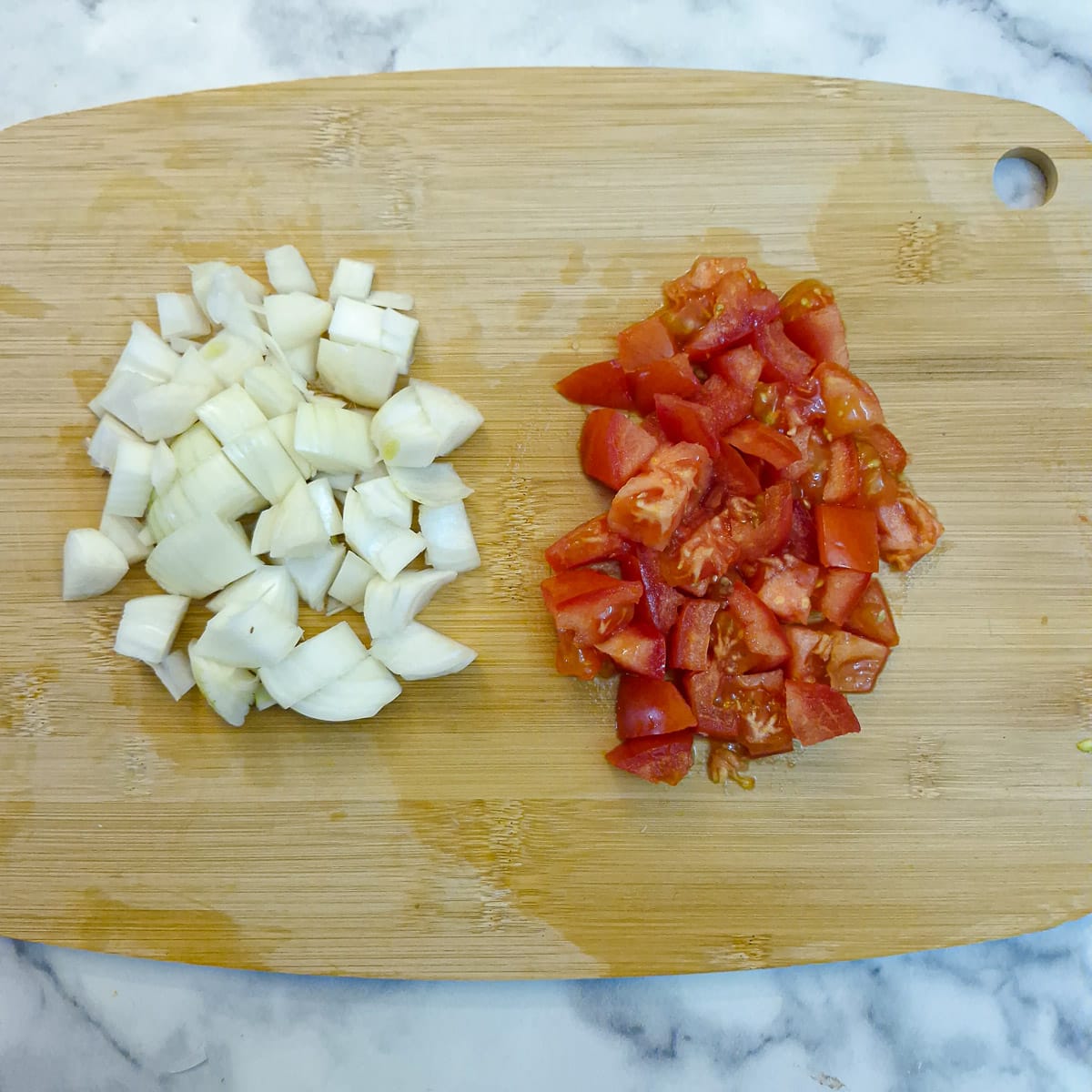 Chopped tomatoes and onions on a wooden chopping board.