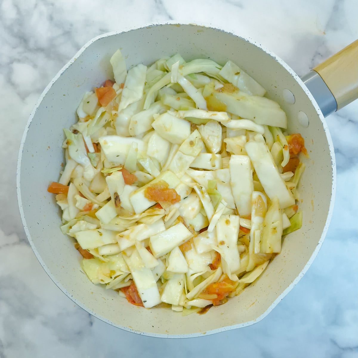 The onions and tomatoes have been stirred through the cabbage in the saucepan.