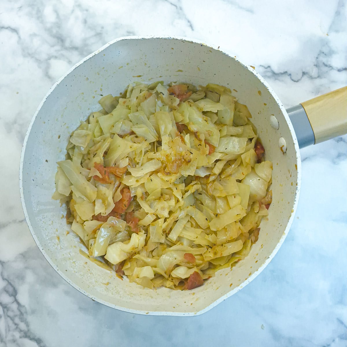 Tomato-braised cabbage in a saucepan. The cabbage has wilted to about one-third of the original volume.