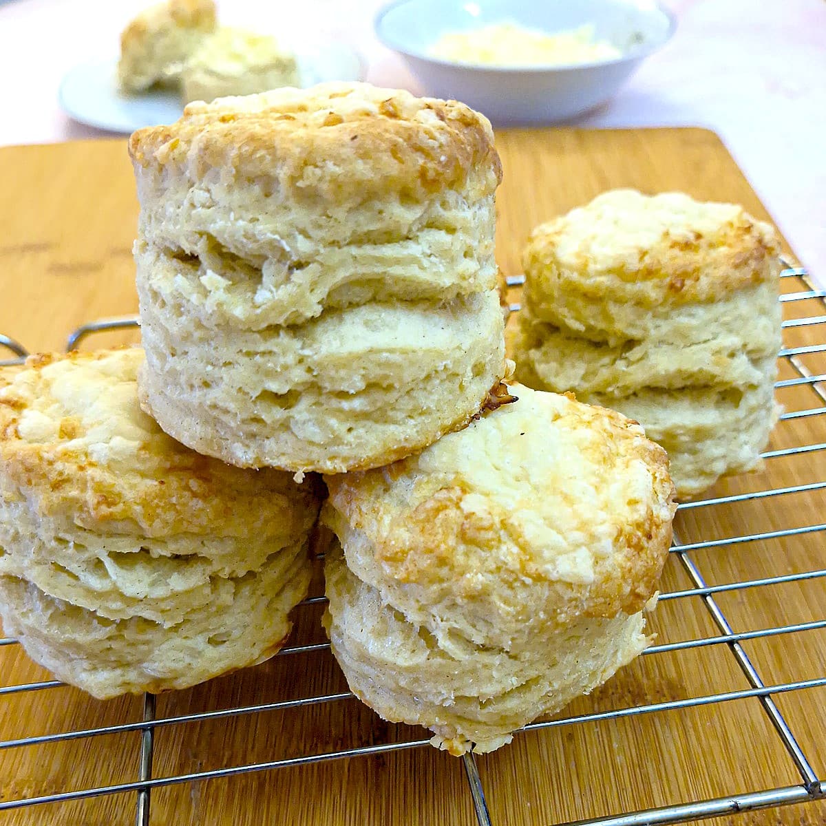 Three high-rise cheese scones piled up on a cooling rack. There are more scones in the background.