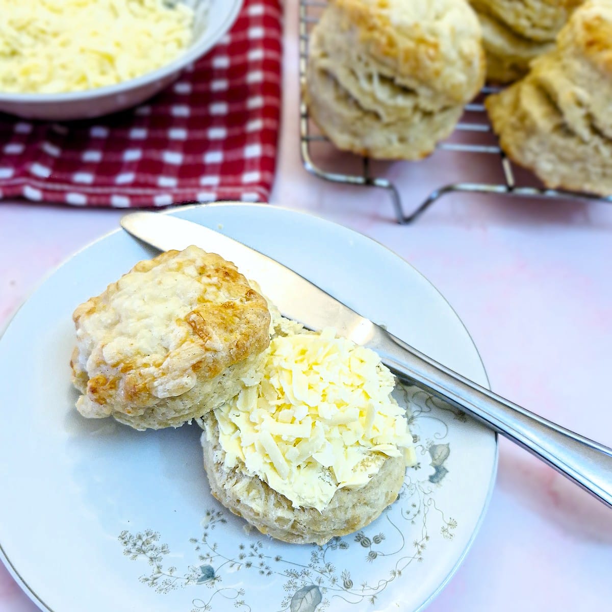 Half a buttered cheese scone topped with grated cheese. The top half of the scone is propped up against the bottom half.