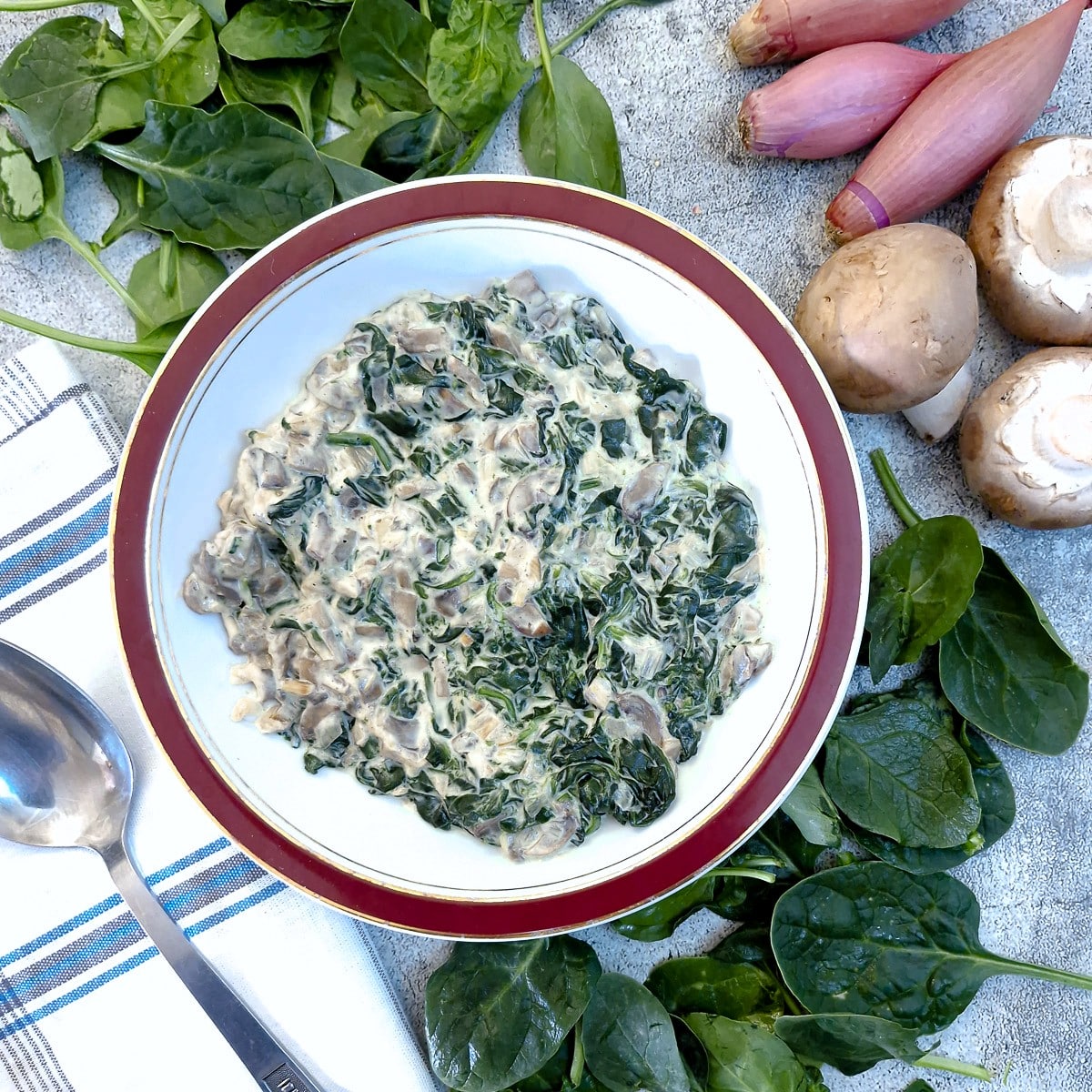 A dish of spinach and mushrooms with cream cheese sauce.
