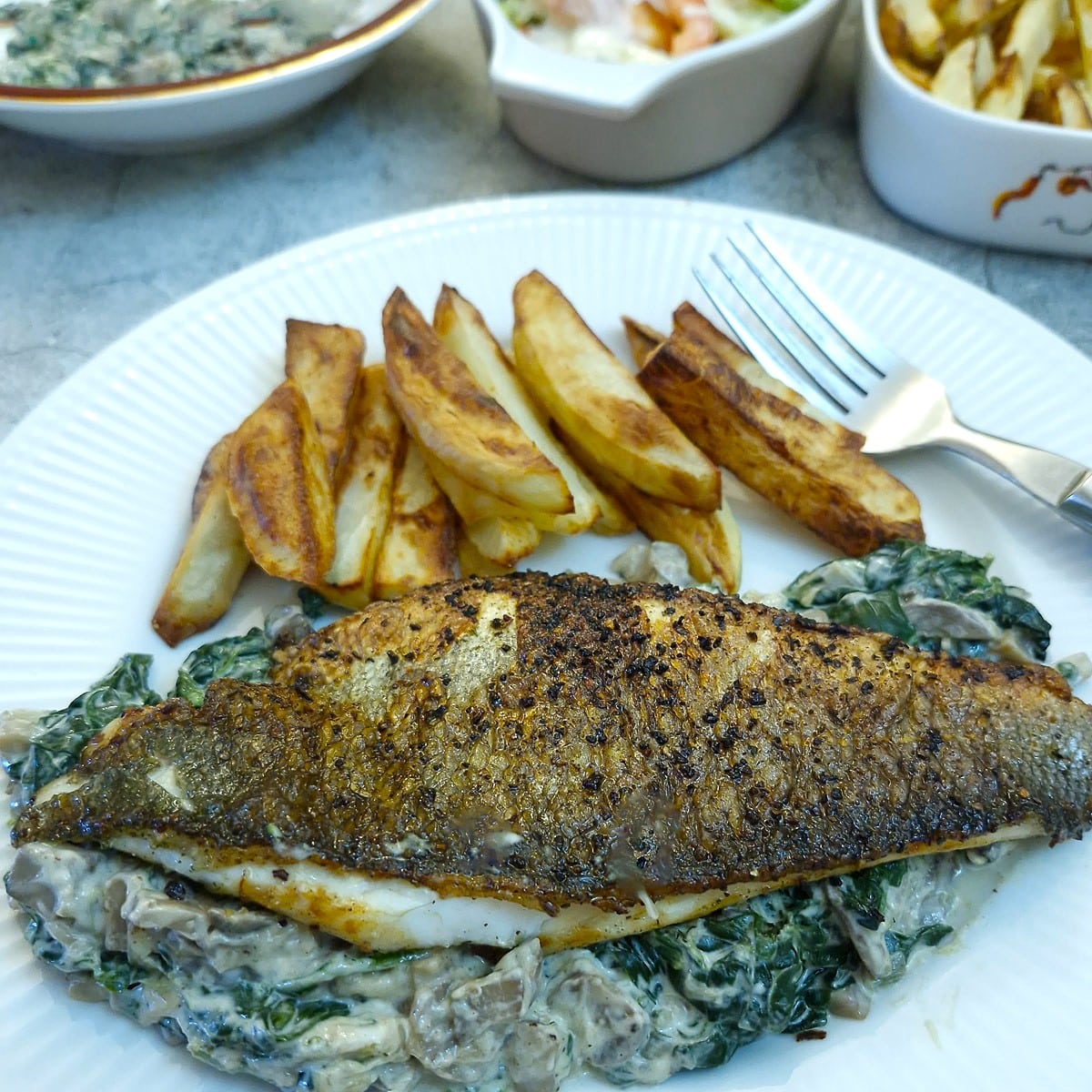 A browned sea bass fillet with crispy skin on a bed of creamed spinach with a few air-fryer chips on the side.