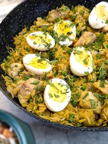 A frying pan filled with curried fish and rice pilaf. There are halved hard-boiled eggs arranged on top, and the entire dish is garnished with chopped coriander.