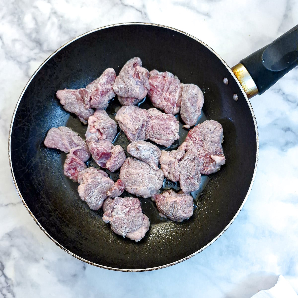 Pieces of flour-coated lamb browning in a frying pan.