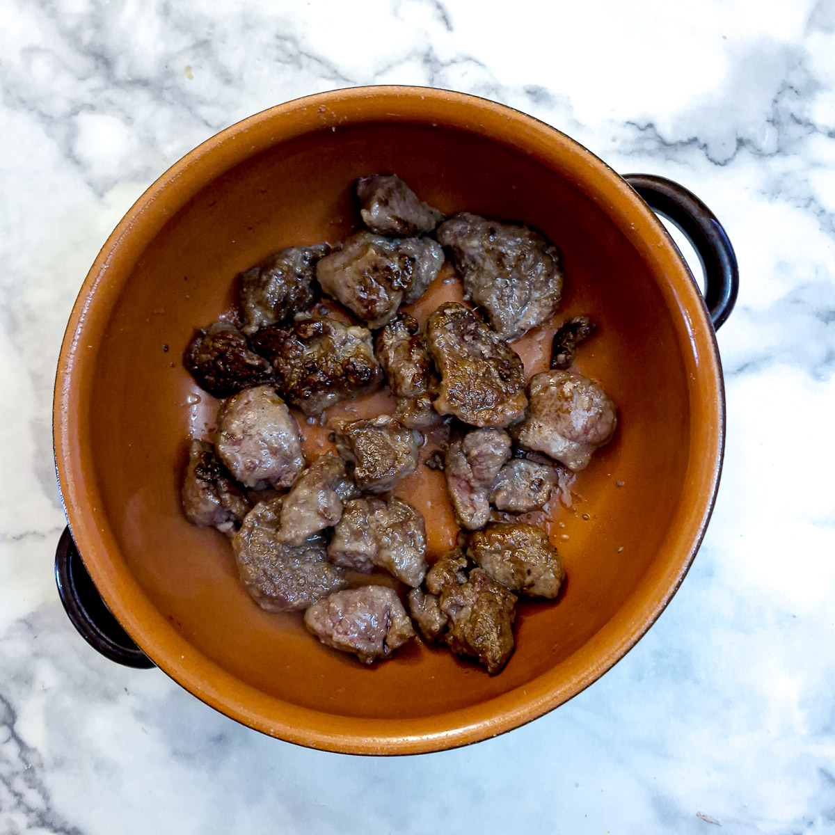 A casserole dish containing browned lamb chunks.