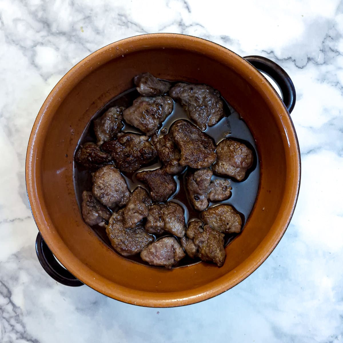 Red wine and spices poured over the lamb in a casserole dish.