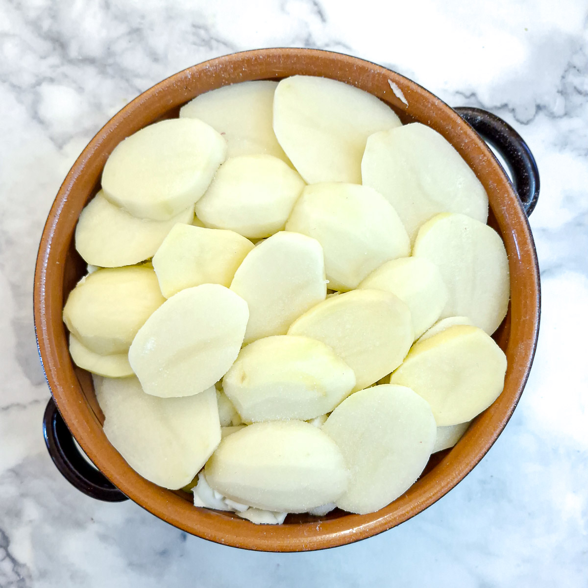 A final layer of thickly sliced potatoes on top.