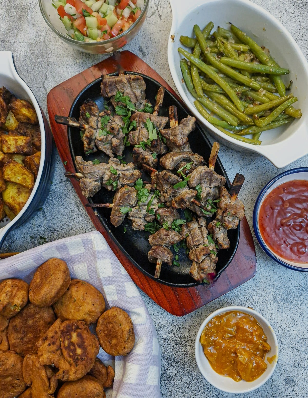 A dish of tandoori lamb skewers on a table, surrounder by side dishes and dips.
