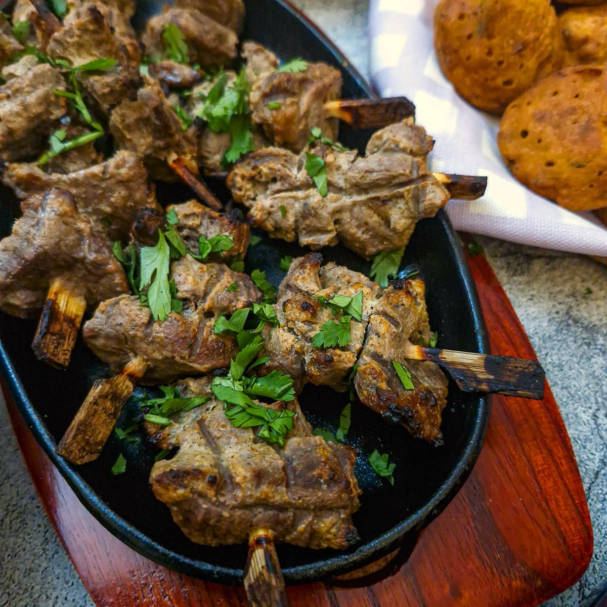 Close-up of a tandoori lamb skewers on a black cast iron plate on a wooden platter.