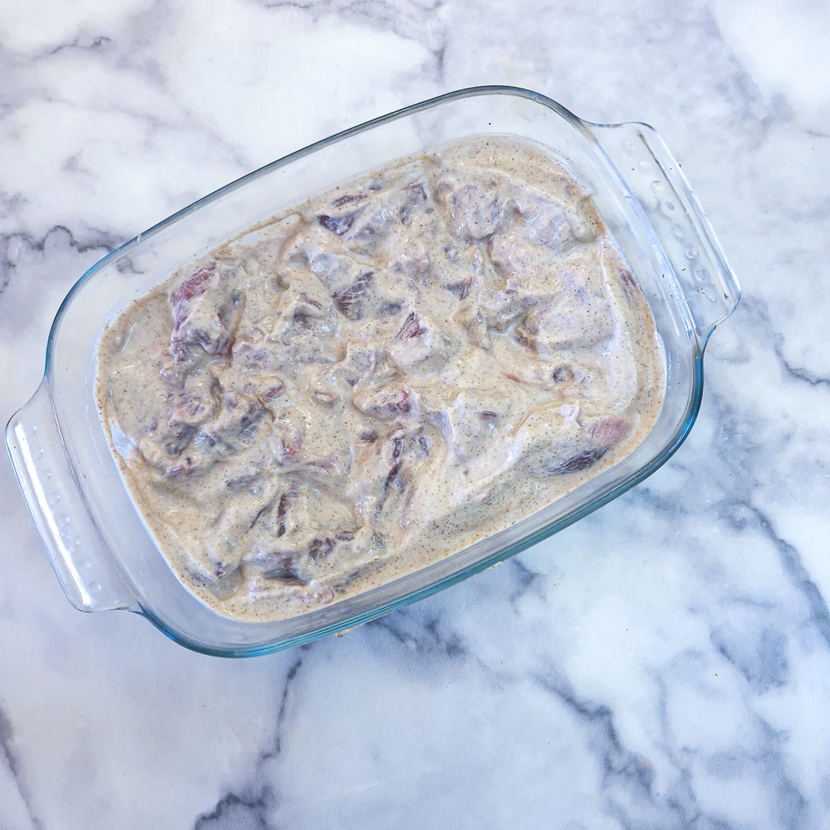 Cubes of lamb leg marinating in a glass dish in yoghurt and spices.
