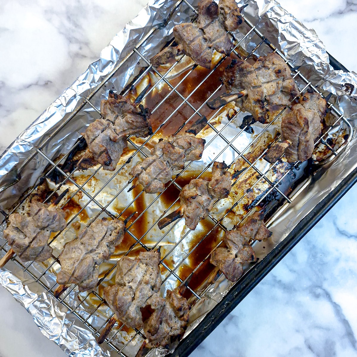 Fully cooked tandoori lamb skewers on a metal rack over a baking tray.