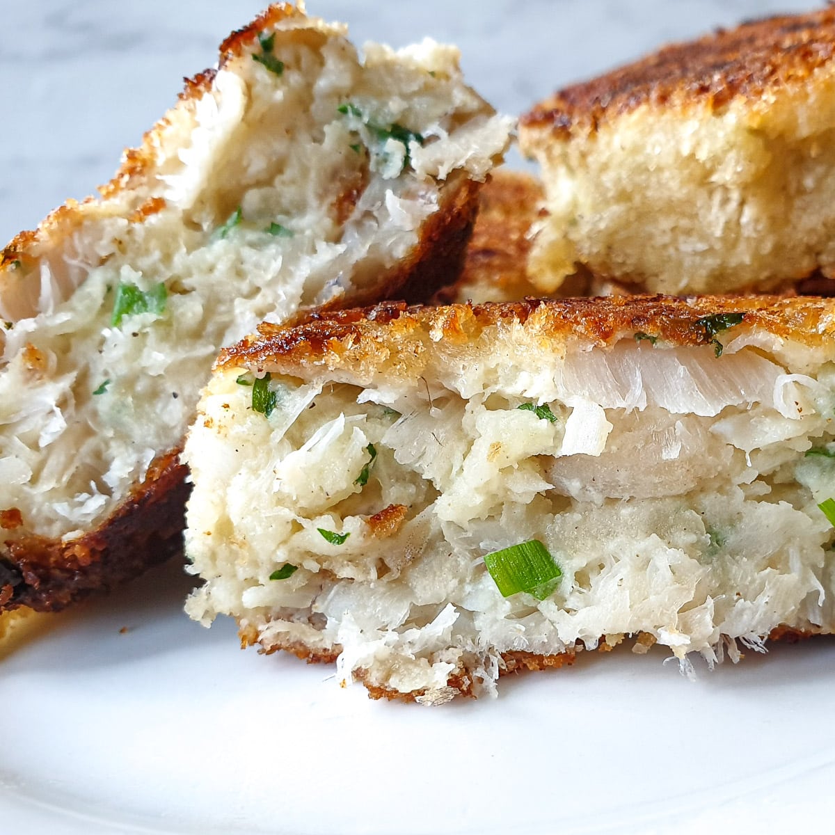 Fish cakes on a white plate. One of them has been cut in half to show the texture.