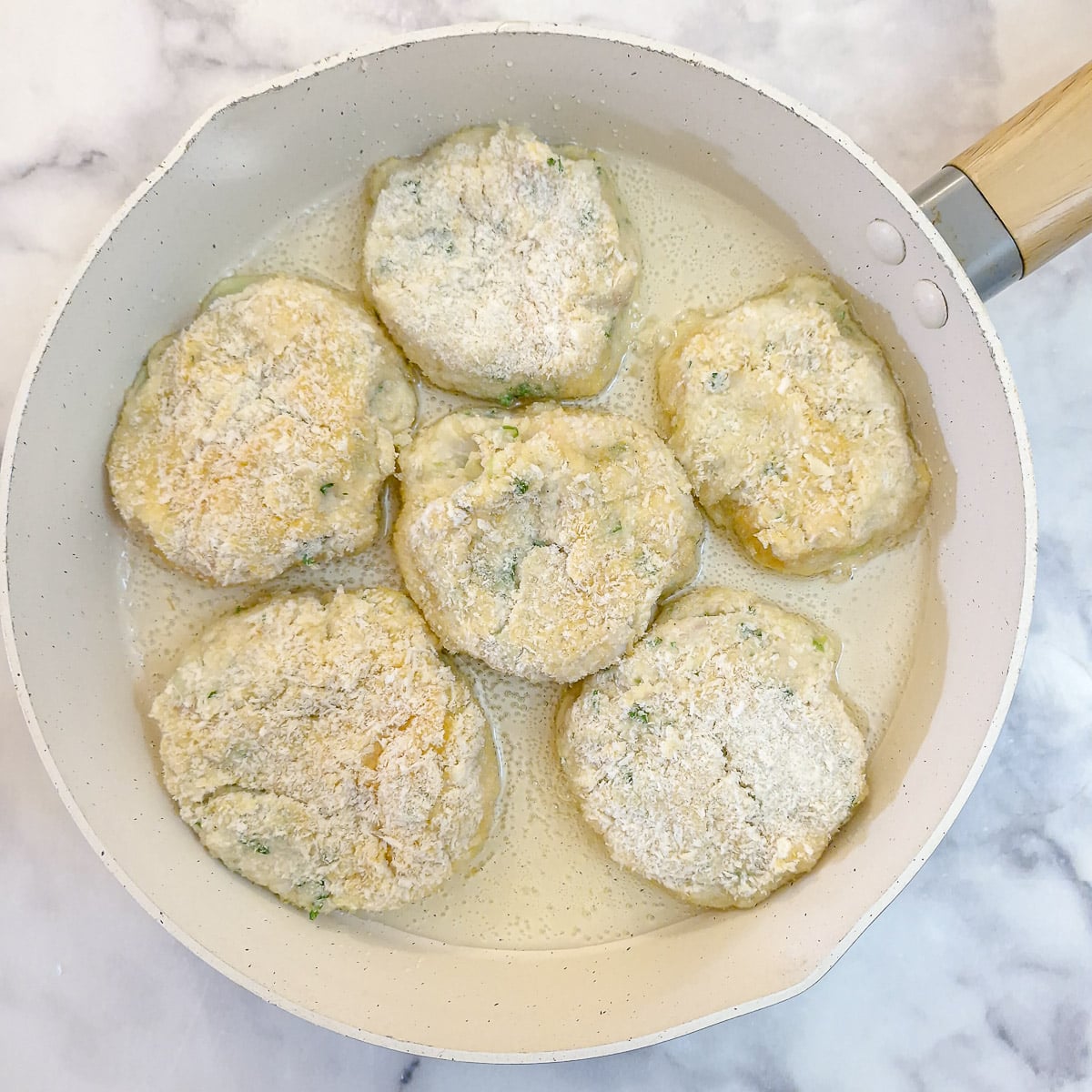 6 uncooked fish cakes in oil in a frying pan.