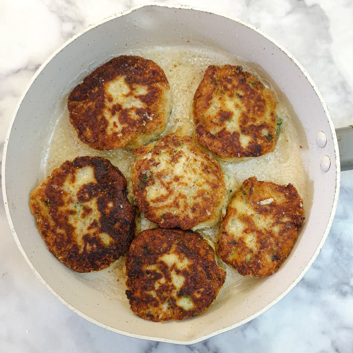 6 cooked and browned fish cakes in a frying pan.