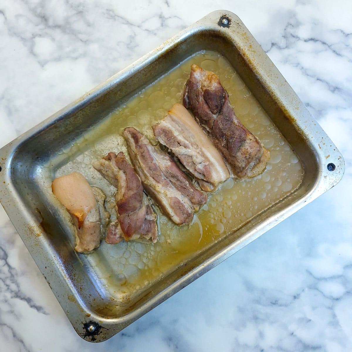 5 cooked pork belly slices in the baking tray. They have lost quite a lot of volume due to the fat having rendered out.